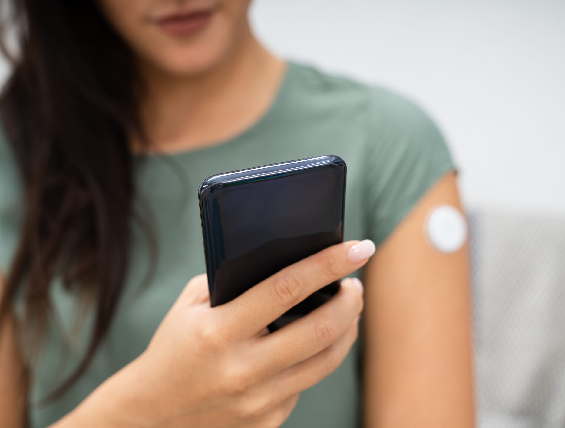 Image shows a woman holding a cellphone while she tracks her blood sugar with her glucose monitor on her arm